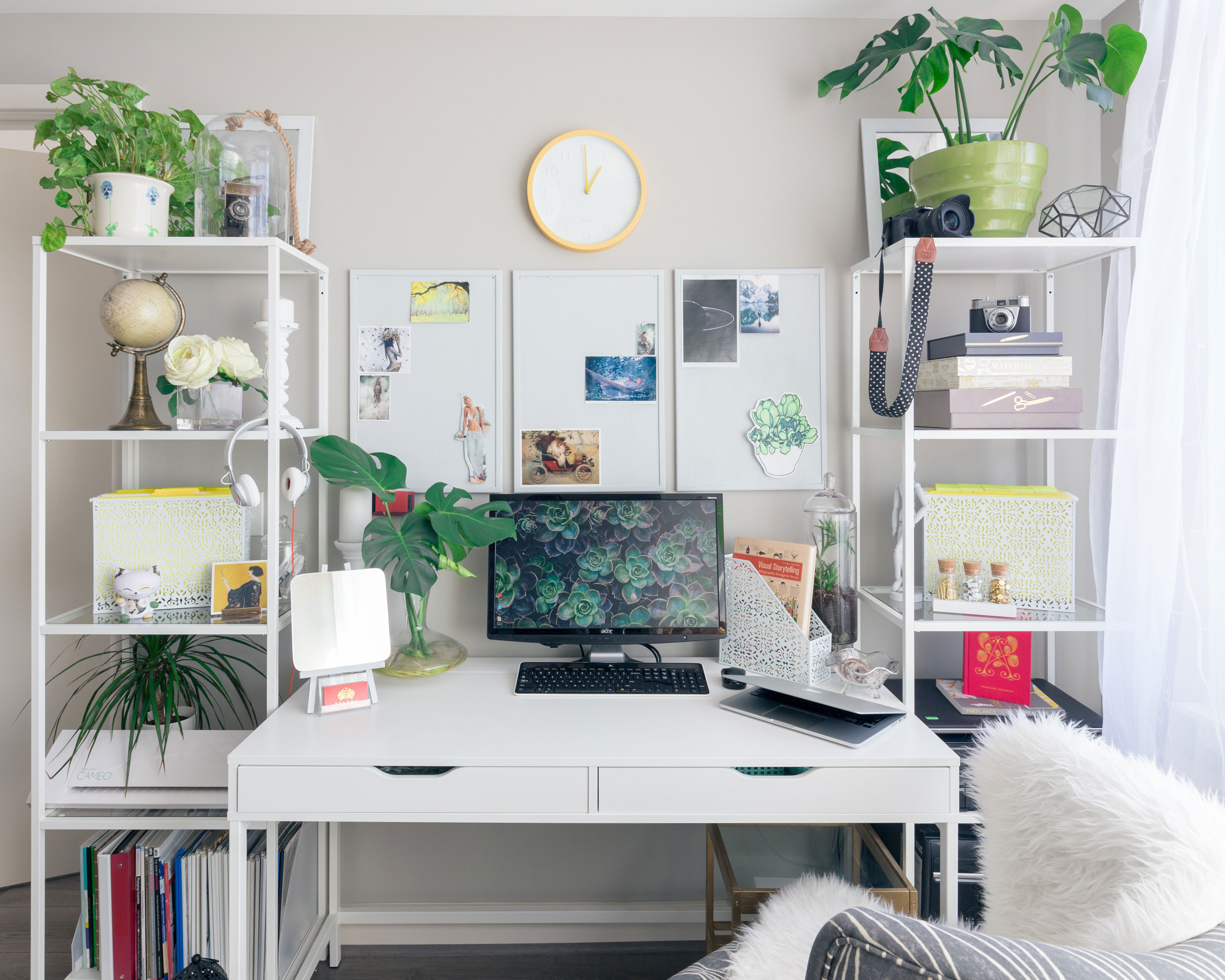 Bright home office setup with a turned on flat screen monitor on a white wooden desk surrounded by plants and shelves Bright home office setup with a turned on flat screen monitor on a white wooden desk surrounded by plants and shelves