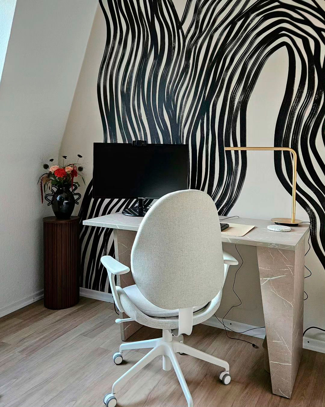 Home office setup featuring a monitor opposite a black and white accent wall with a modern chair and desk. Home office setup featuring a monitor opposite a black and white accent wall with a modern chair and desk.