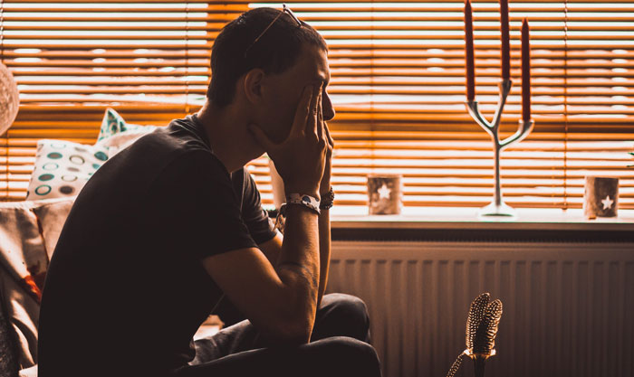 Man sitting with head in hands indoors, reflecting after visiting mom to introduce baby son and facing family intervention. Man sitting with head in hands indoors, reflecting after visiting mom to introduce baby son and facing family intervention.