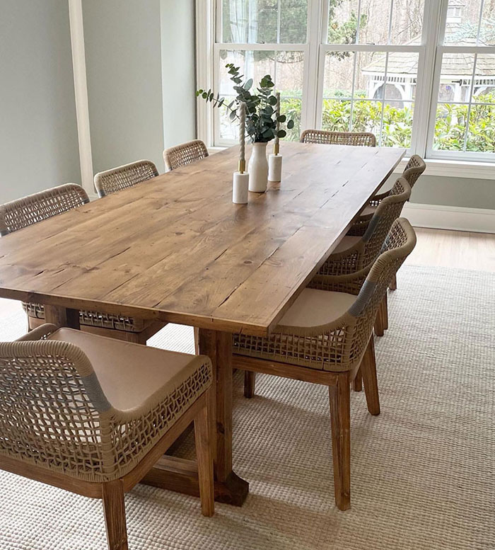 Provincial colored wooden dining table with natural wood stain color in a bright, well-lit room with wicker chairs. Provincial colored wooden dining table with natural wood stain color in a bright, well-lit room with wicker chairs.