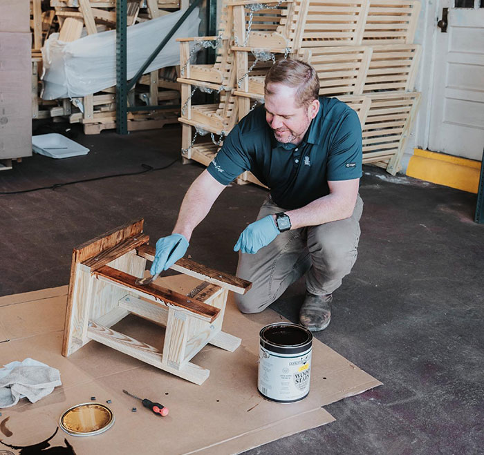 Man applying wood stain to a chair, demonstrating Minwax stain colors for choosing wood stain color in a workshop setting. Man applying wood stain to a chair, demonstrating Minwax stain colors for choosing wood stain color in a workshop setting.