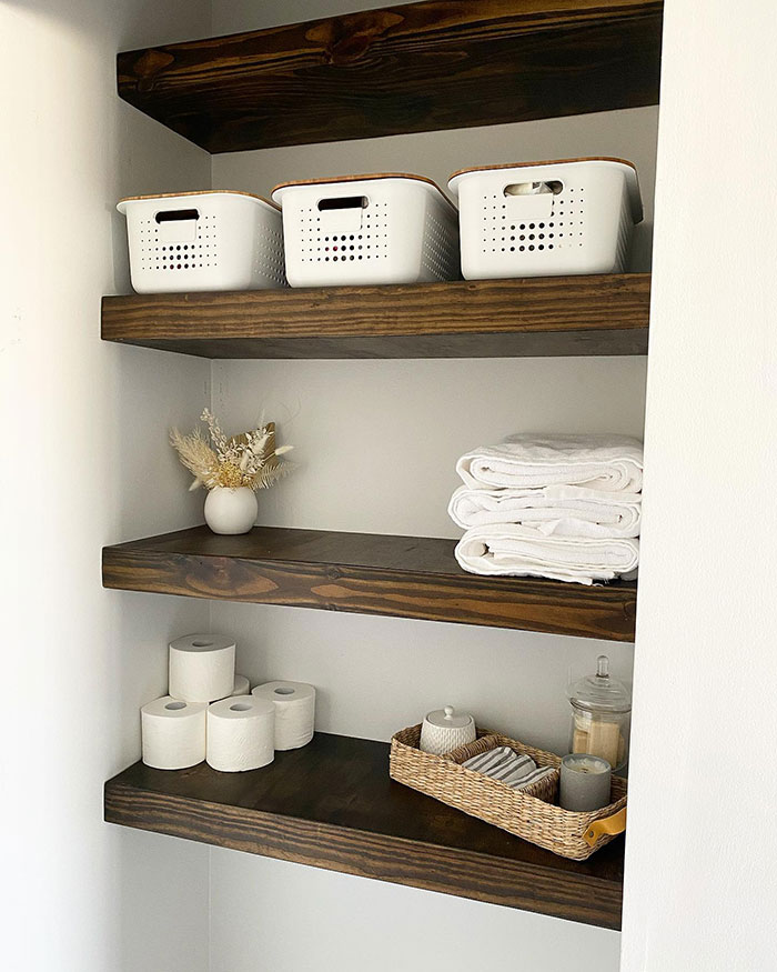 Dark walnut shelves stained in rich Minwax stain colors holding baskets, towels, and bathroom essentials in a corner. Dark walnut shelves stained in rich Minwax stain colors holding baskets, towels, and bathroom essentials in a corner.