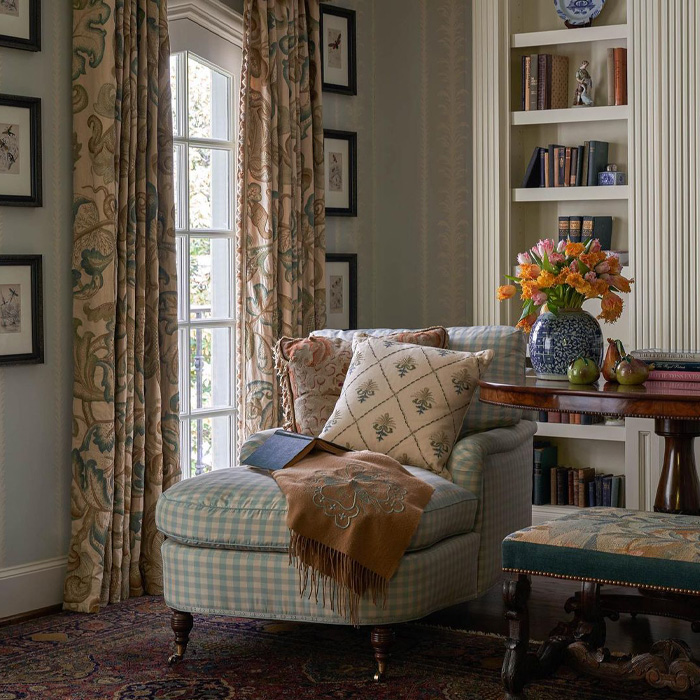 Classic old money interior design featuring a cozy chair with pillows and a blanket next to a window and floral curtains. Classic old money interior design featuring a cozy chair with pillows and a blanket next to a window and floral curtains.