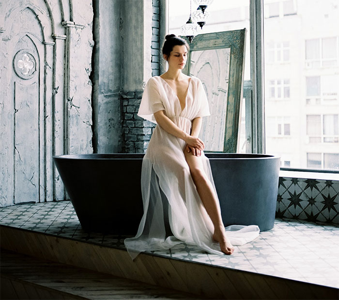 Portrait of woman in dress sitting on bathtub