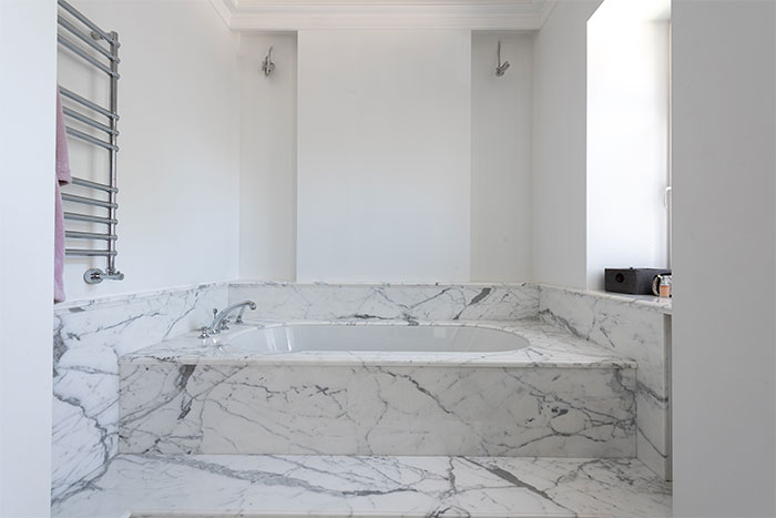 white ceramic bathtub in a marble finish floor and walls