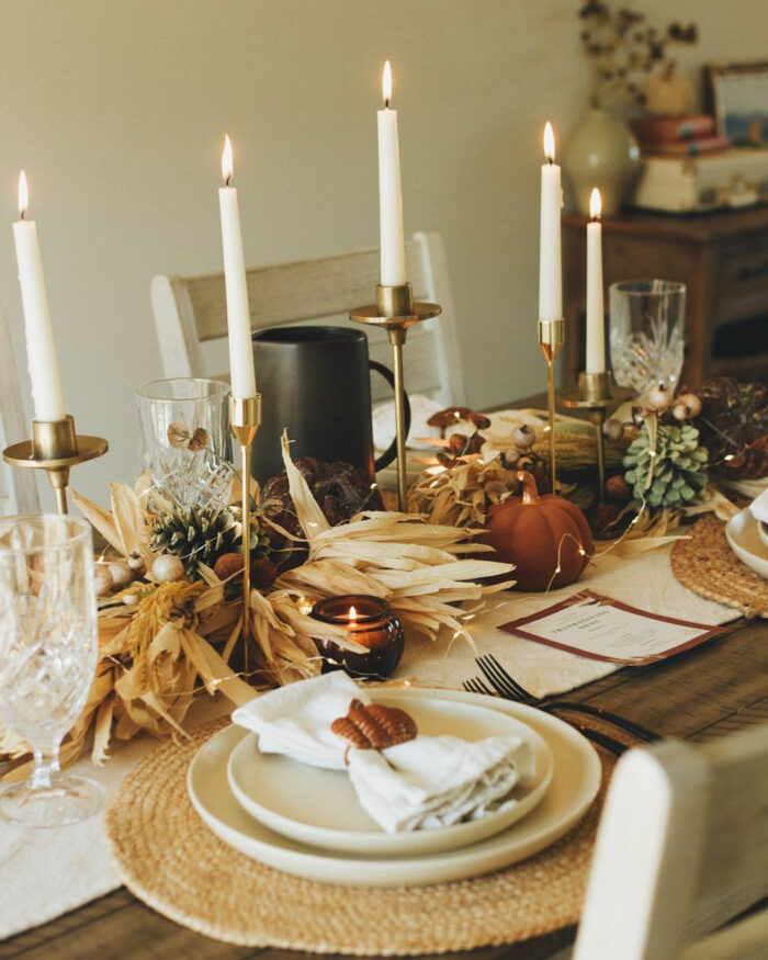 Candlesticks with candles near pumpkins and pine cones on the table