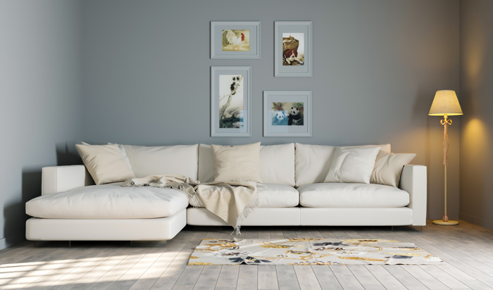 A white couch with pillows on it next to a lamp and images on the wall