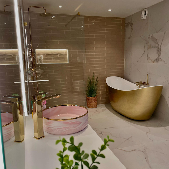 A bathroom with golden bathtub and pink sink 