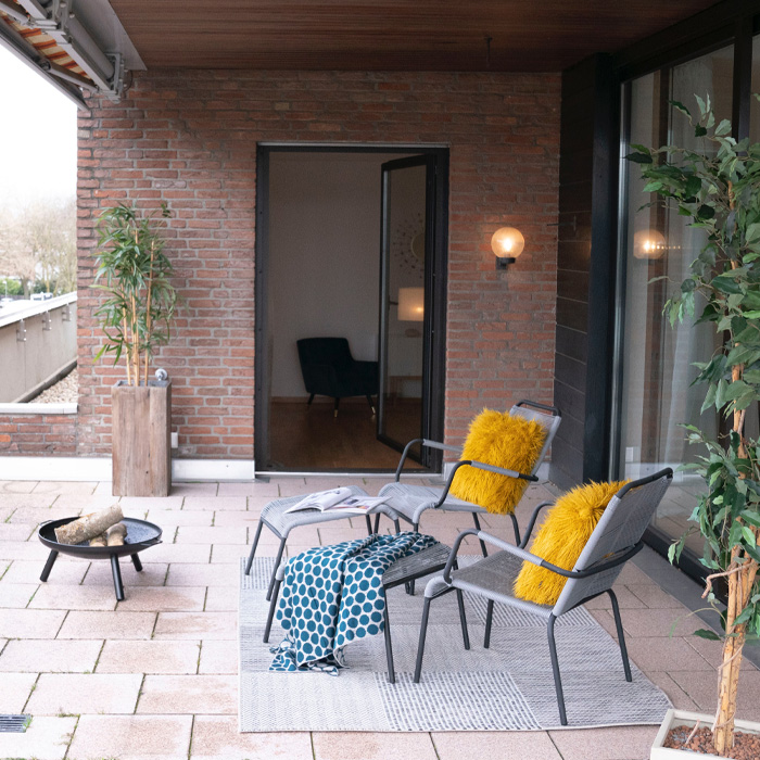 Grey patio chairs with warm yellow pillows and a cozy fire pit, illustrating warm colors in outdoor decor ideas. Grey patio chairs with warm yellow pillows and a cozy fire pit, illustrating warm colors in outdoor decor ideas.