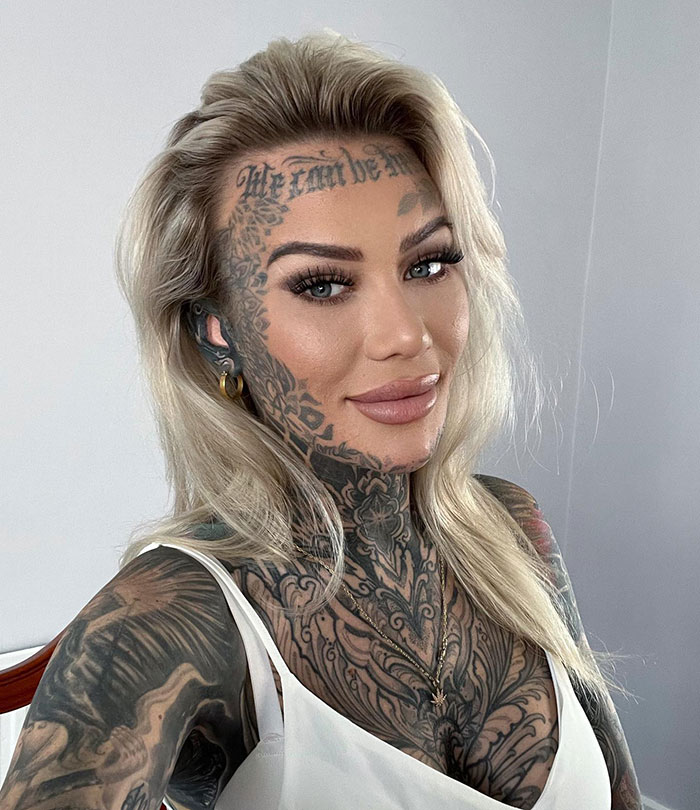 Influencer with tattooed forehead smiling, intricate facial and neck tattoos, long blonde hair, wearing a white top. Influencer with tattooed forehead smiling, intricate facial and neck tattoos, long blonde hair, wearing a white top.