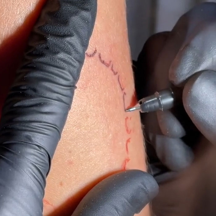 Tattoo artist inking arm, symbolizing love, using a tattoo machine while wearing black gloves. Tattoo artist inking arm, symbolizing love, using a tattoo machine while wearing black gloves.