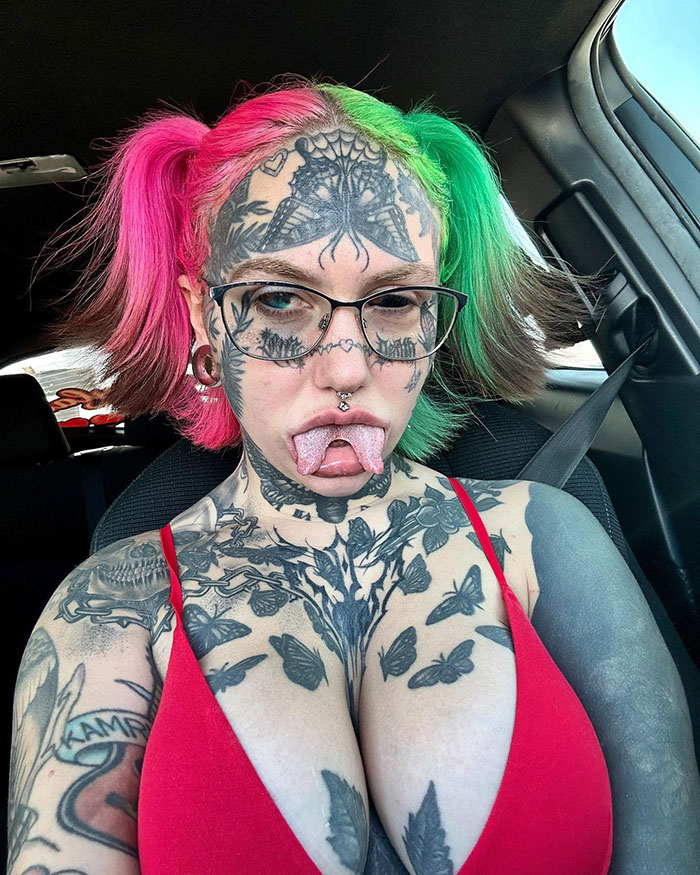 Tattooed woman with vibrant hair and facial piercings in a car, showcasing modified look. Tattooed woman with vibrant hair and facial piercings in a car, showcasing modified look.
