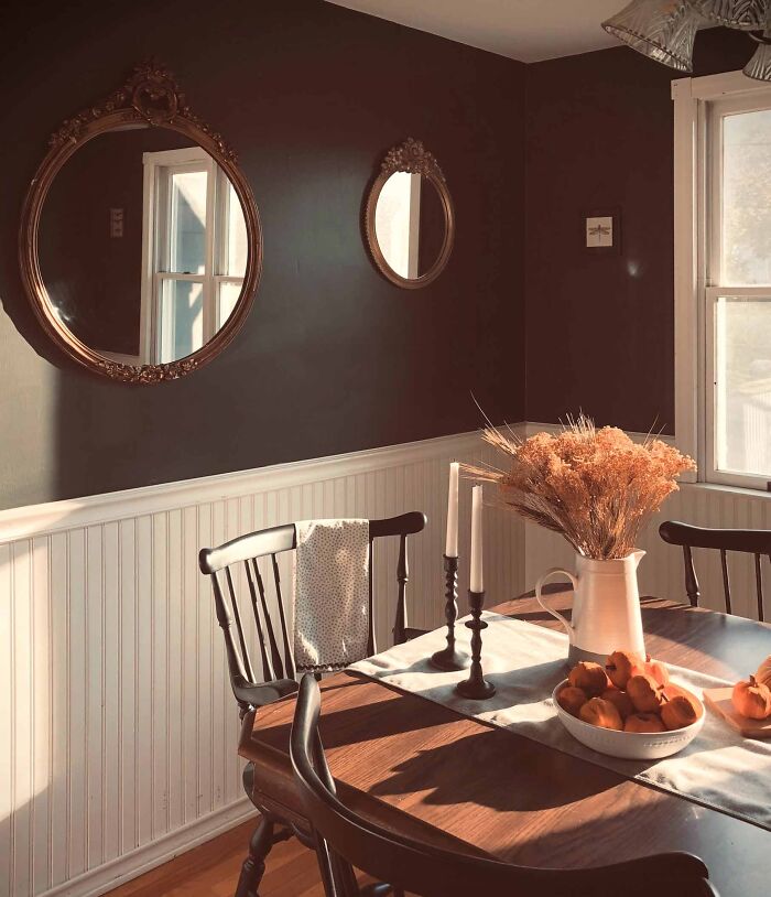 Dining room with dark painted walls, white wainscoting and wooden table