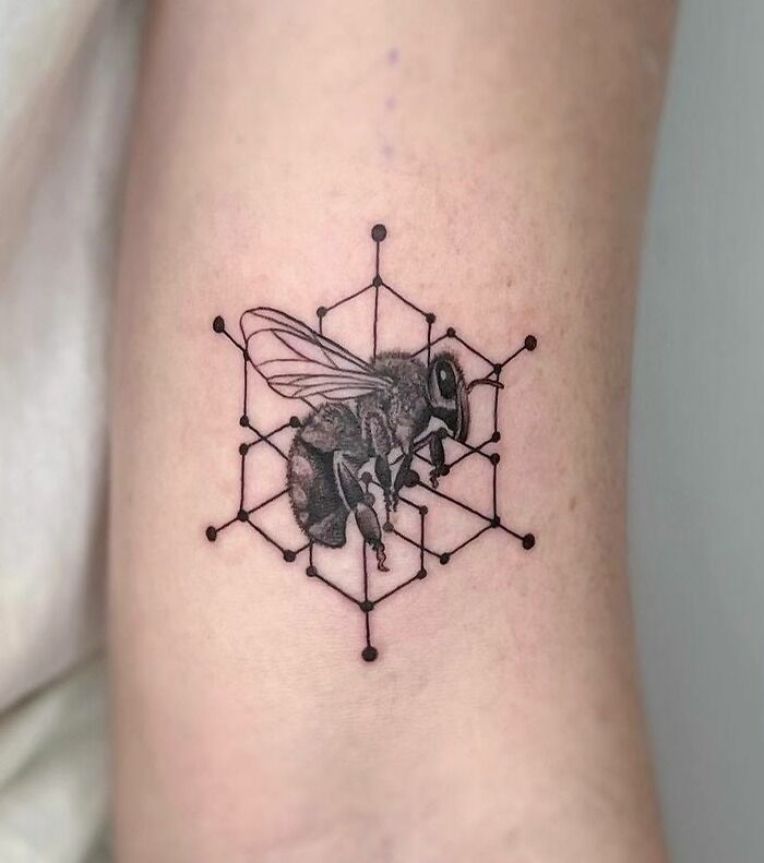 Realistic and geometric black bee and hexagon tattoo on arm