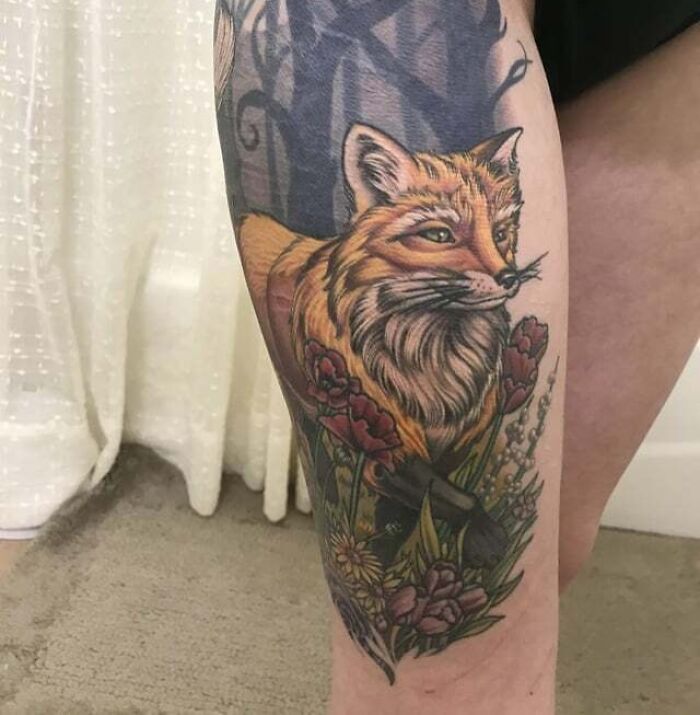 Vibrant fox tattoo on leg, surrounded by flowers and foliage, showcasing creative animal tattoo design.