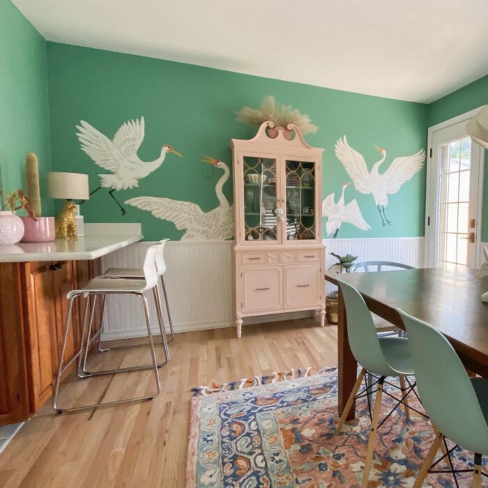 Green dining room with bird murals on walls, pastel cabinet, wooden table with chairs, showcasing dining room ideas.