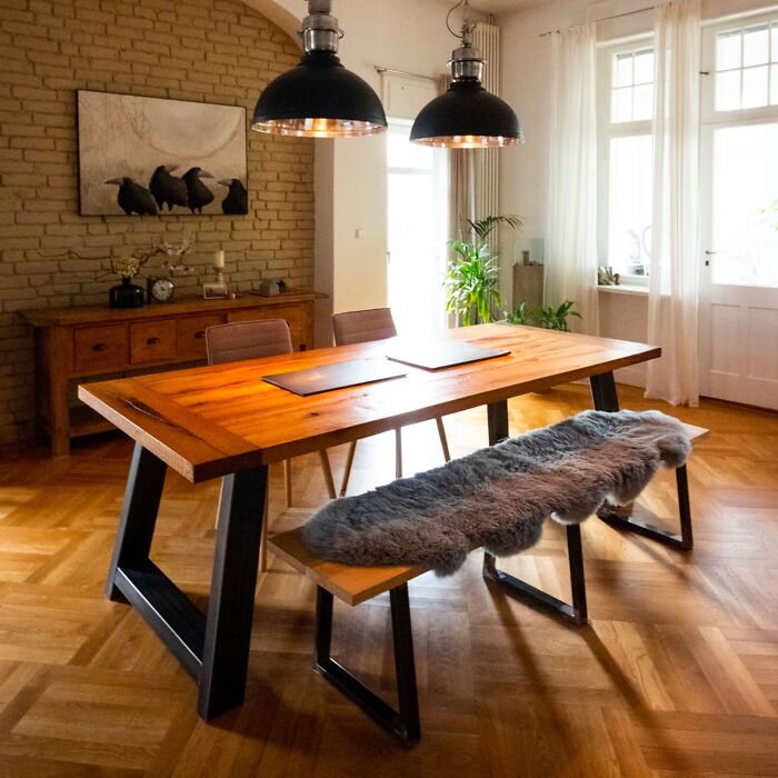 Rustic dining room with wooden table and bench featuring cozy fur throw and modern lighting for family gatherings.