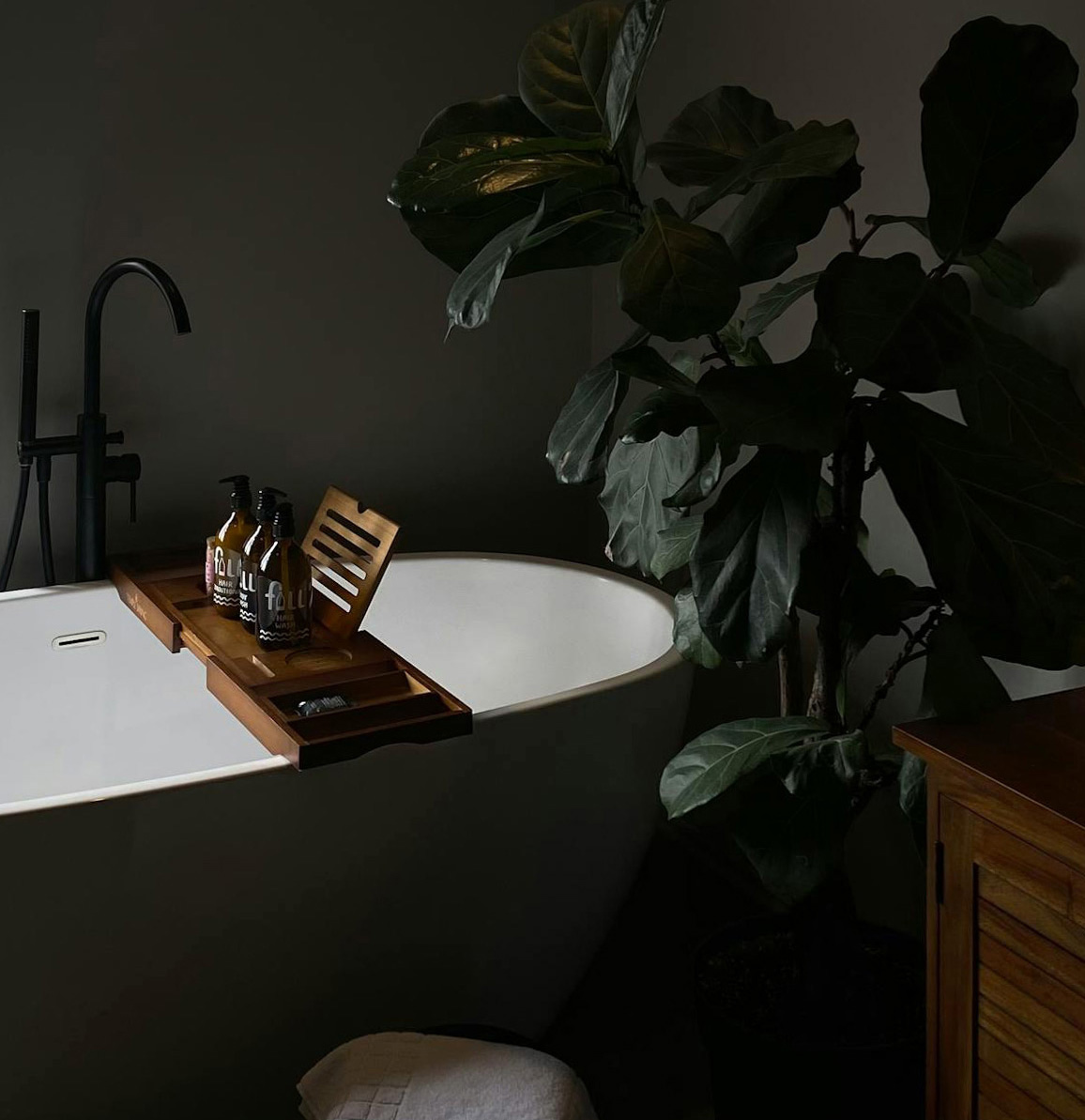 Black bathroom with white tub and plant
