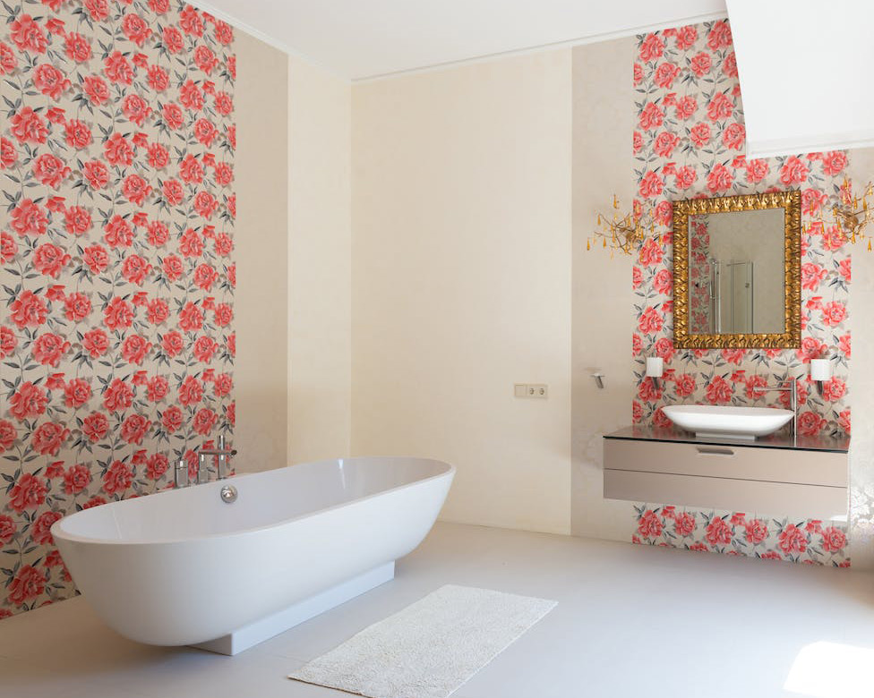 Light sand color bathroom with red rose tapestries, white tub, mirror, and light bath rug