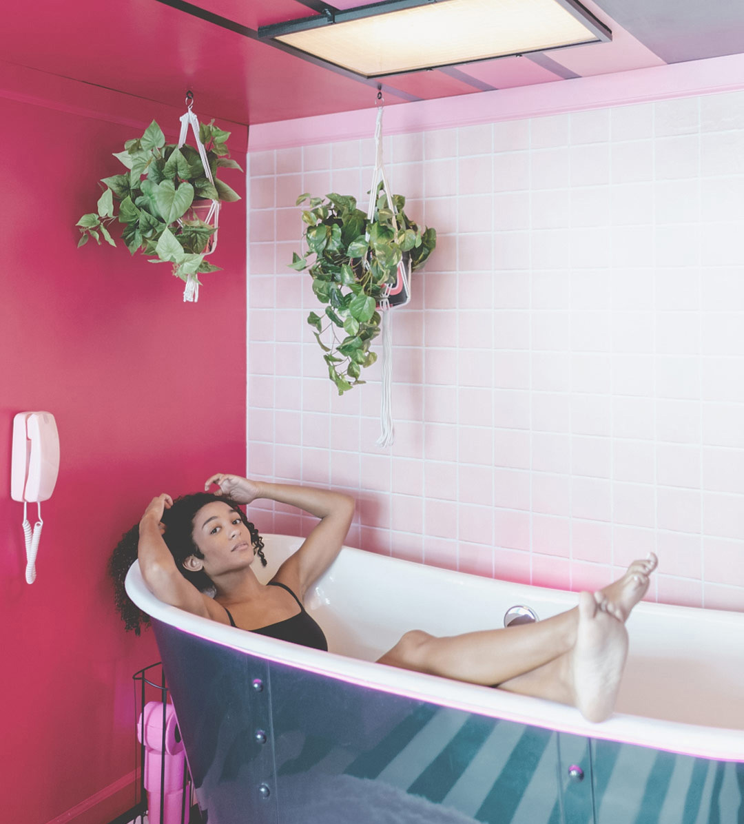 Razzle Dazzle pink bathroom with a young woman in the tub and two hanging plants