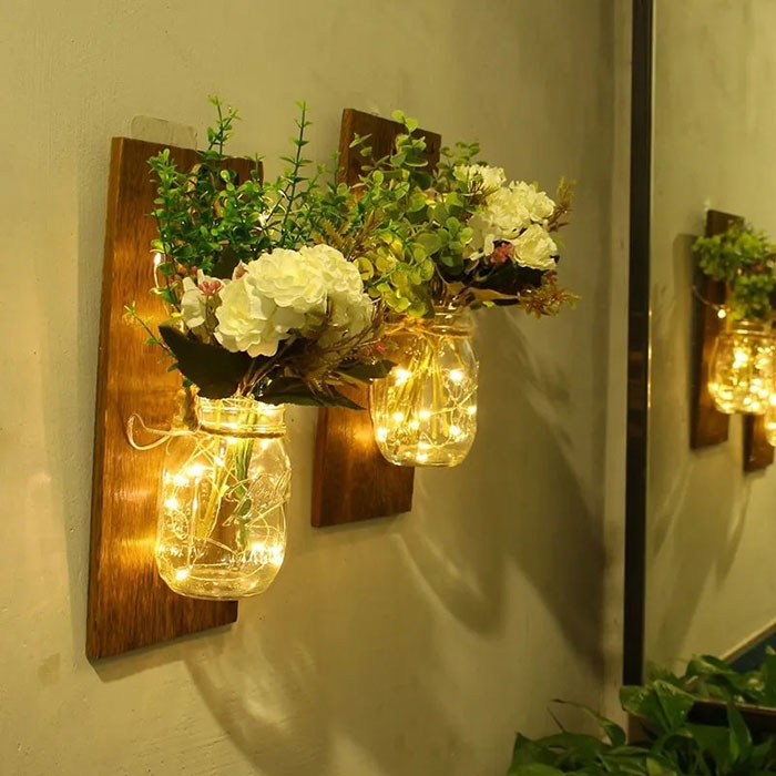 Two mason jars on wall with lights and flowers inside