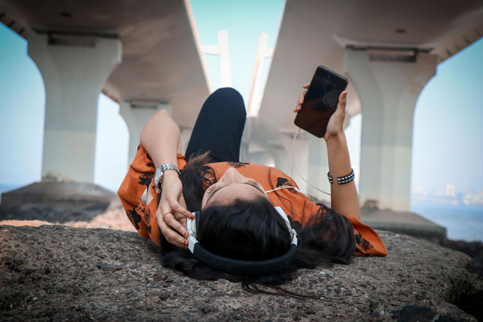 Woman laying on ground and listening music under a bridge 