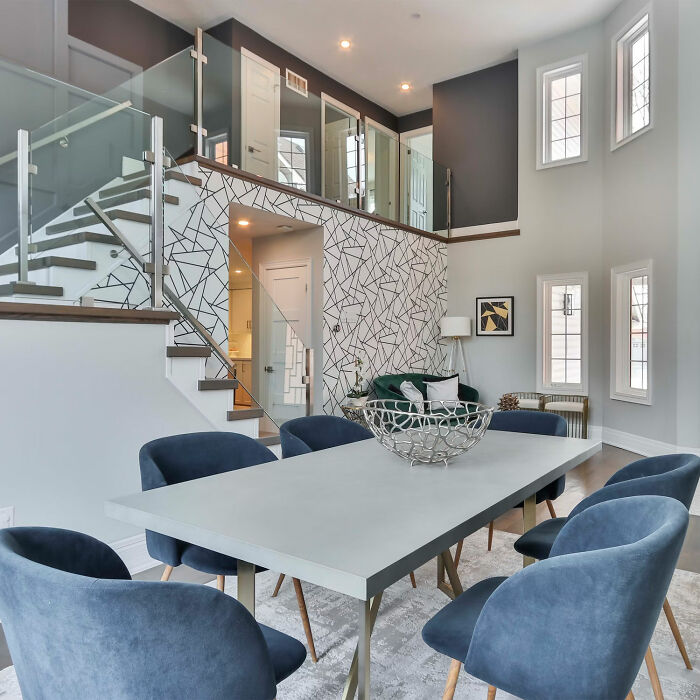 Dining room with blue chairs and white table in a modern space featuring stairs and geometric wall art.