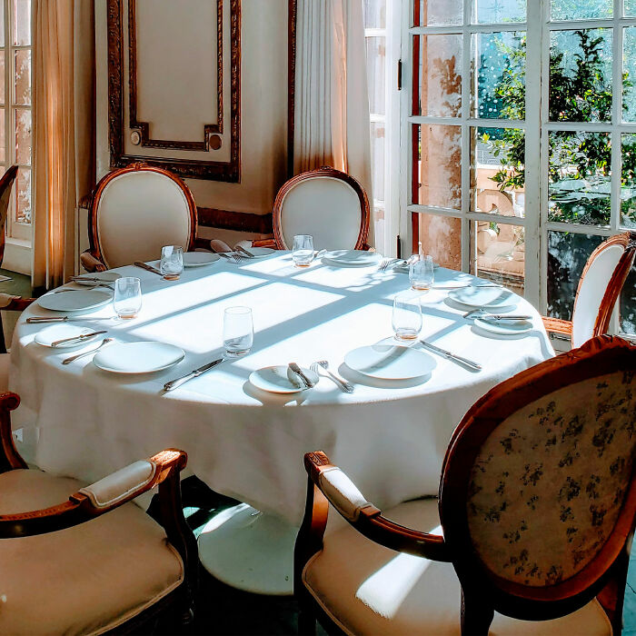 Round dining table with white tablecloth and classic chairs near sunlit window, showcasing inspiring dining room ideas.