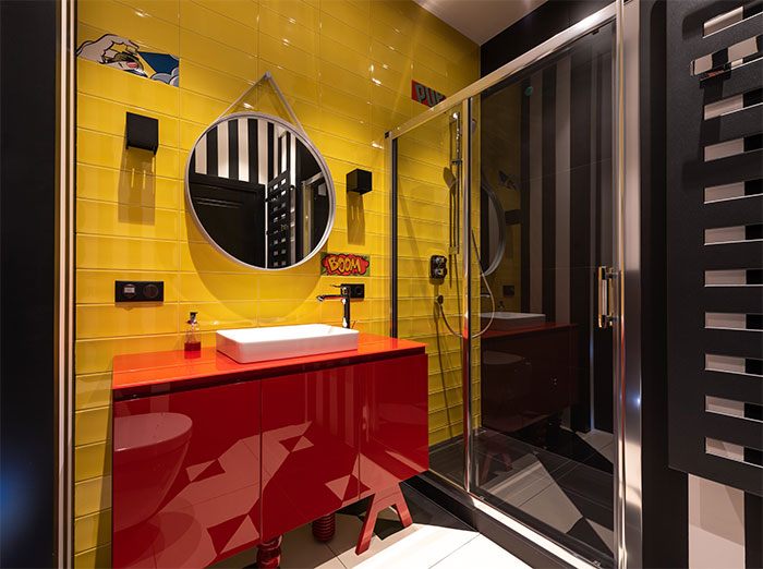 A bathroom with glossy bright yellow tiles, a red cabinet, and mirror