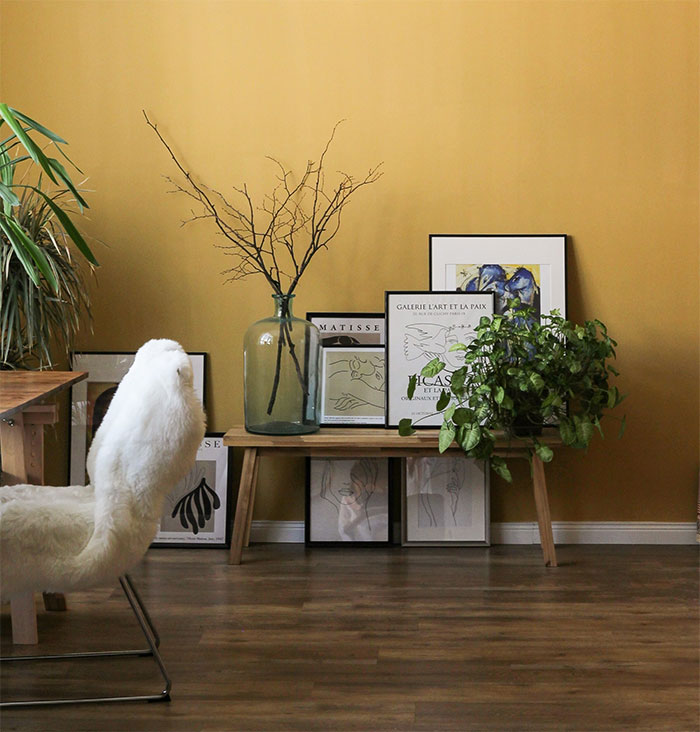 A pale yellow room with a fluffy white chair and paintings on the ground