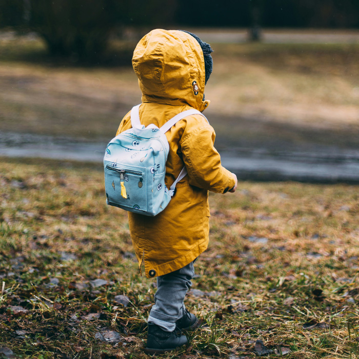 A kid wearing yellow jacket and blue backpack 