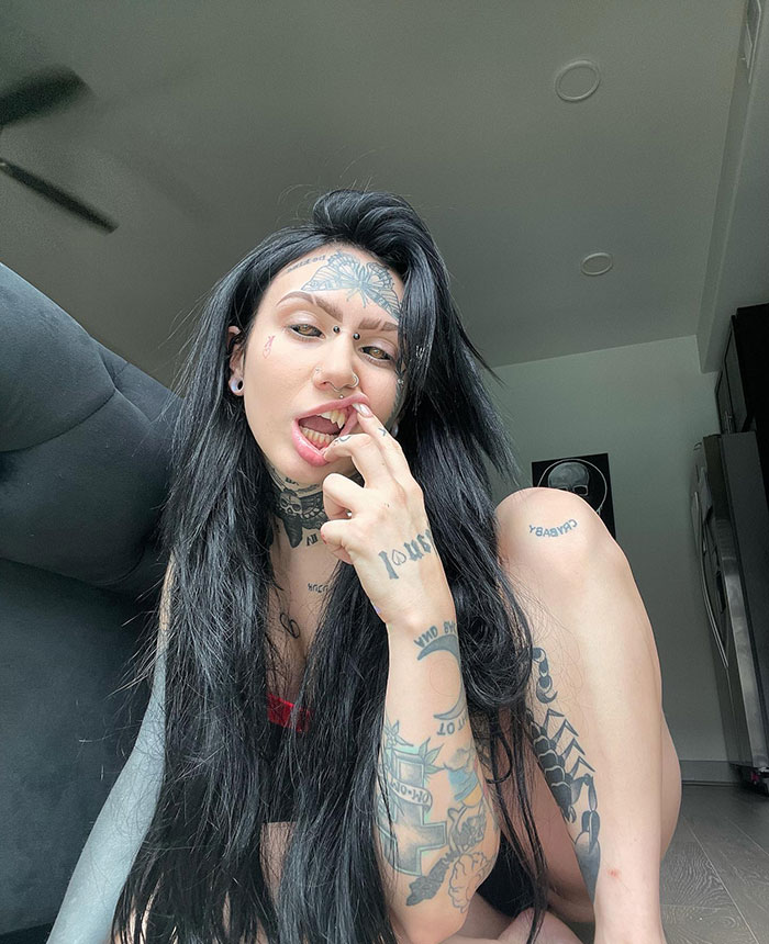 Woman with extensive body modifications and tattoos, sitting indoors. Woman with extensive body modifications and tattoos, sitting indoors.