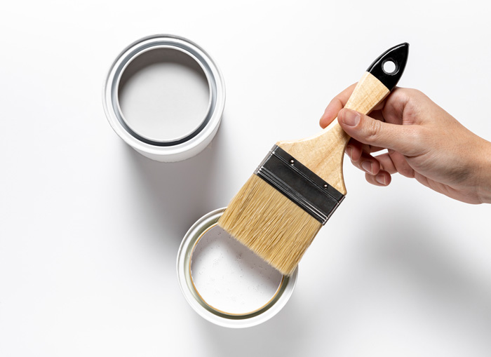 A hand holding a brush over white can of paint 