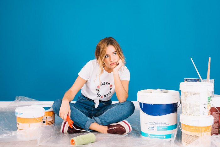 Woman holding roller sitting in front of a painted wall 