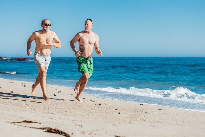 Two men running shirtless on the beach 
