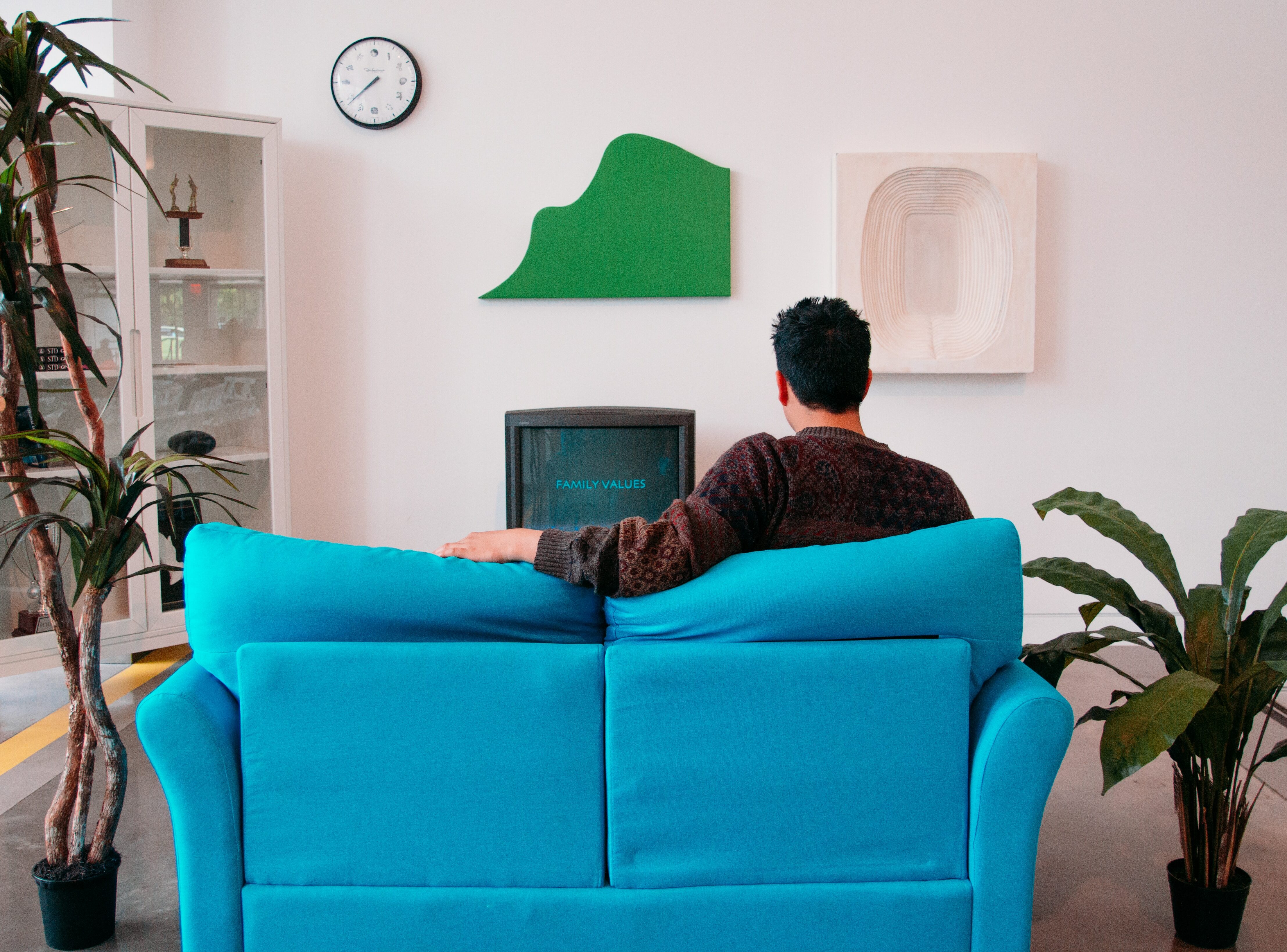 Man sitting ant small blue couch and watching tv