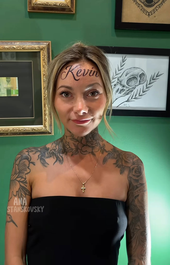 Influencer with fake forehead tattoo of boyfriend's name, surrounded by framed art. Influencer with fake forehead tattoo of boyfriend's name, surrounded by framed art.