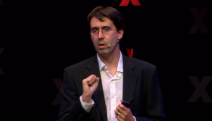 Scientist discusses the longevity bottleneck and dinosaur impact while holding a talk. Scientist discusses the longevity bottleneck and dinosaur impact while holding a talk.