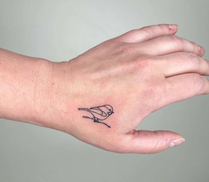 A simple black linear bird tattoo on the hand