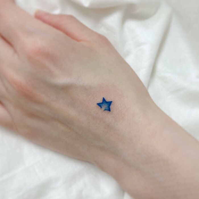 Blue small star tattoo on hand