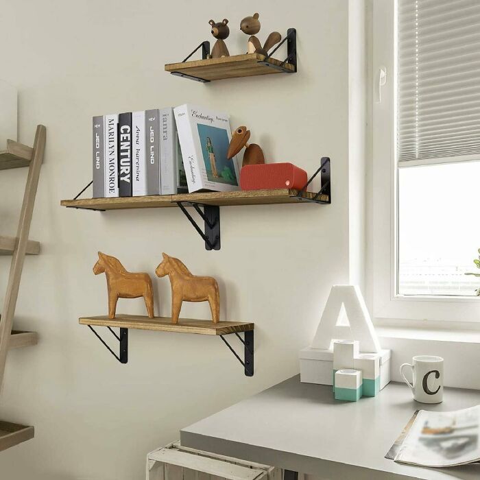 Three wooden floating shelves with books and toys