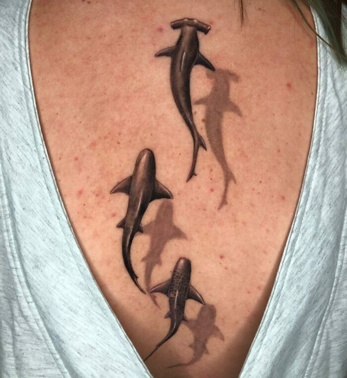 Three realistic sharks with shadows swimming tattoo on a woman's back