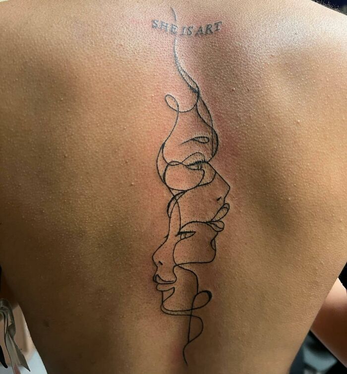 Line art spine tattoo with abstract faces and text "She is art."