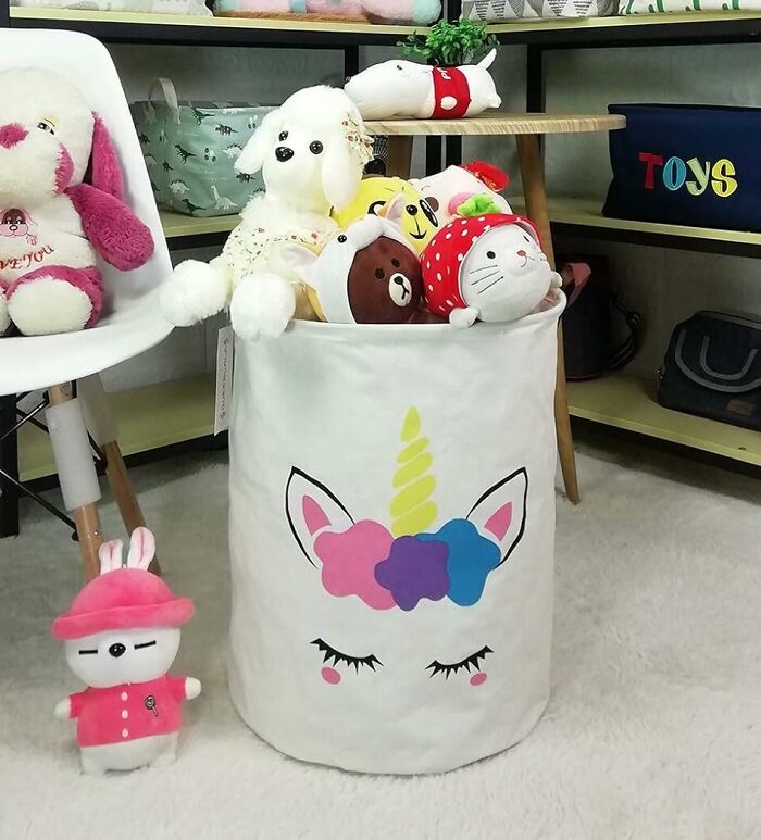 Large white storage basket with colorful unicorn on it and many soft toys in it
