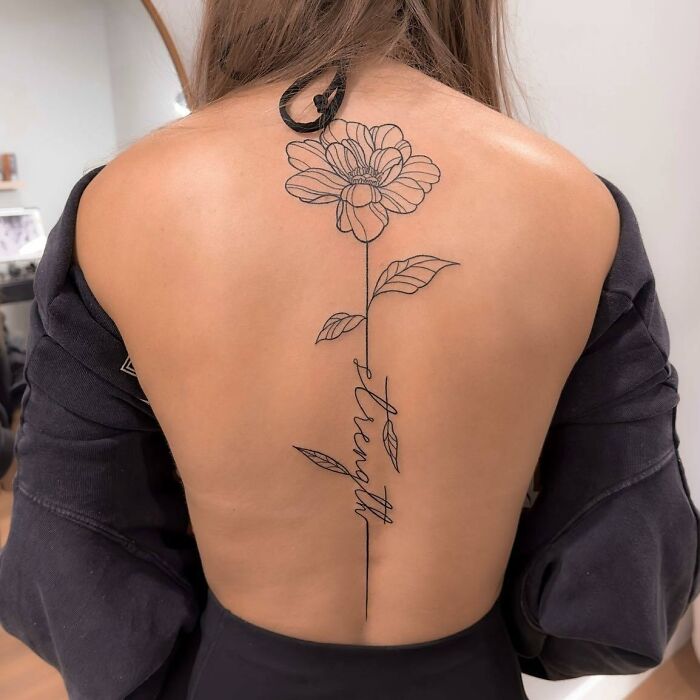 Black linear flower and lettering tattoo on spine