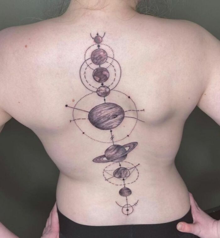 Back displaying intricate spine tattoo of planets and celestial designs.