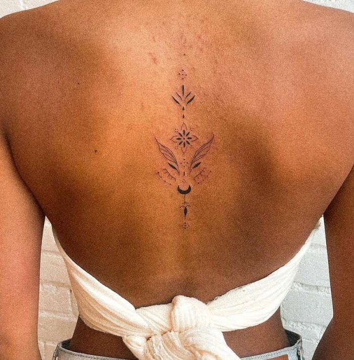 Minimalist floral spine tattoo design on a woman's back with a white top.