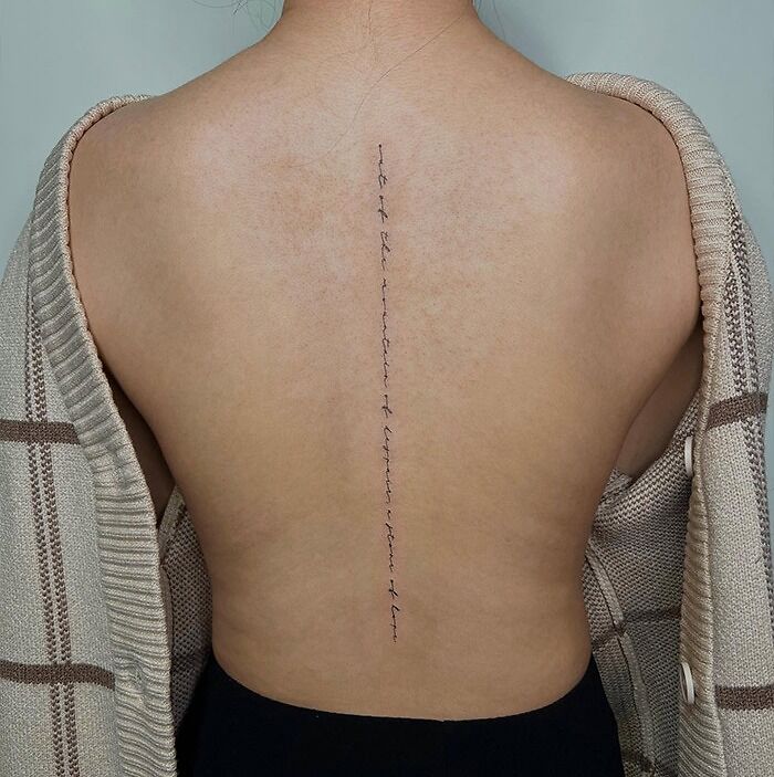 Minimalist spine tattoo running down the back, framed by a draped cardigan.