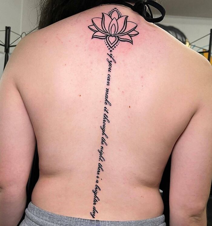 Black vertical lettering and lotus flower on top tattoo on spine