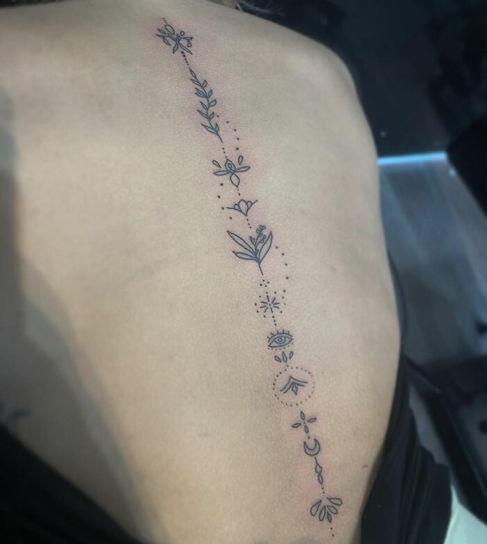 Intricate floral spine tattoo featuring leaves and abstract symbols.